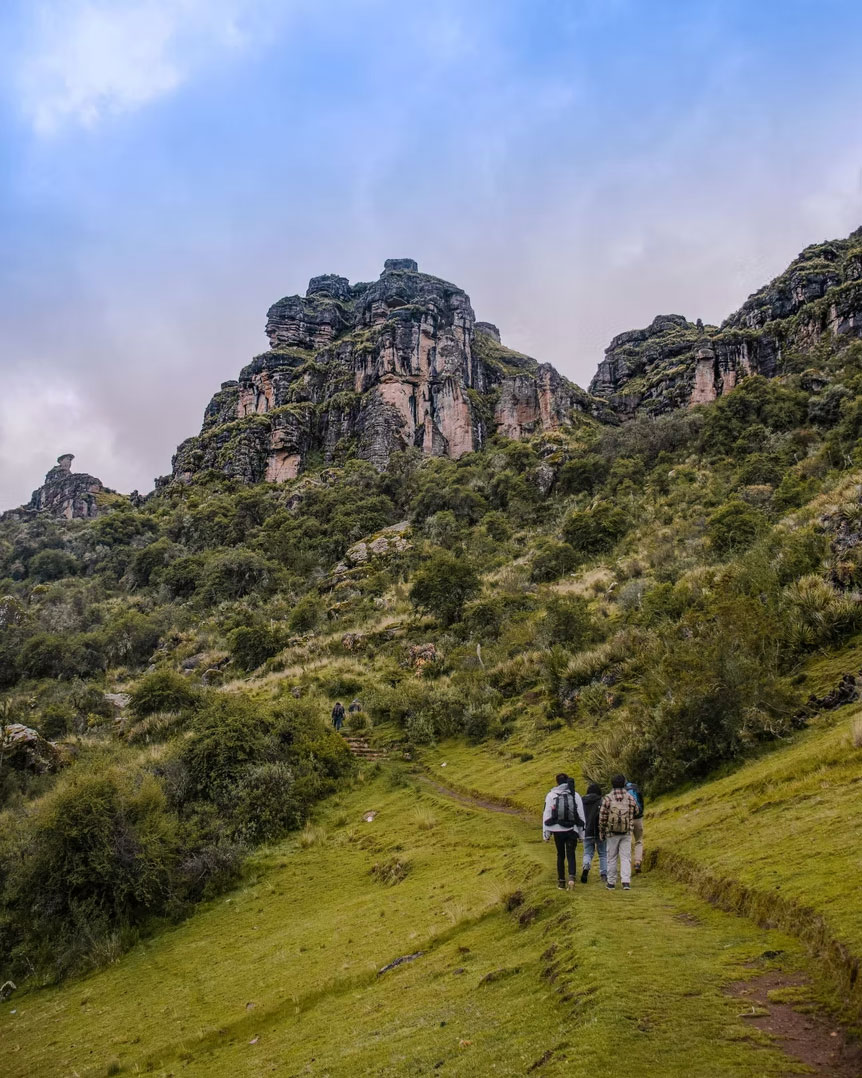 Hikers trekking through a green Andean valley toward rocky cliffs in Peru