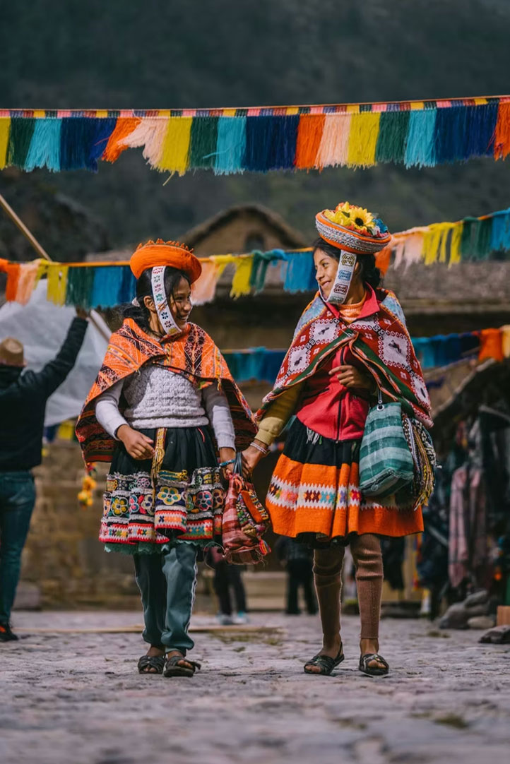 Andean women in traditional clothing walking through a decorated village street